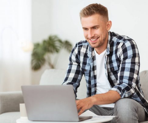 happy-man-using-laptop-sitting-on-couch-JTR57HD